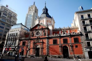 Fachada completa de la Iglesia de la Concepción Real de Calatrava con edificios emblemáticos de Madrid de fondo en la calle Alcalá