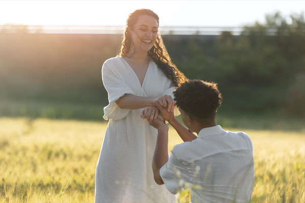 Hombre de color arrodillado pidiendo matrimonio a su novia en un entorno verde con sol de atardecer