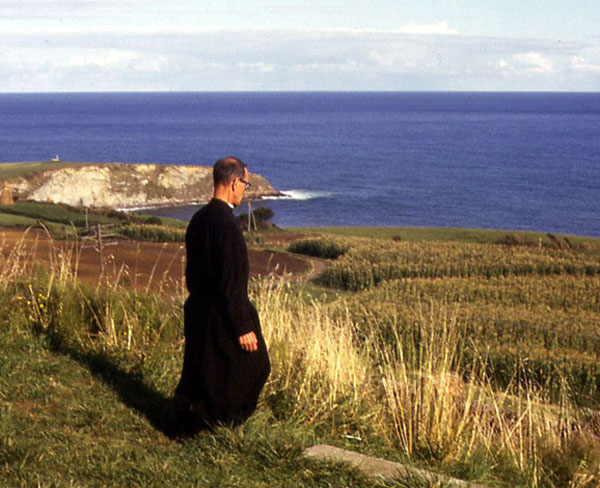 El padre Tomás Morales caminando por la hierba hacia el mar.